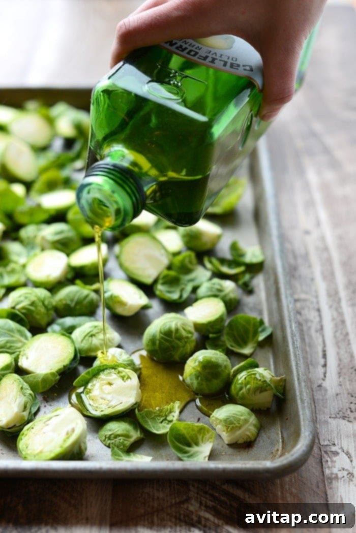 Fresh Brussels sprouts being generously drizzled with olive oil on a baking sheet, ready for roasting.