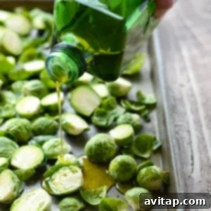 Fresh Brussels sprouts being drizzled with olive oil on a baking sheet, ready for seasoning.
