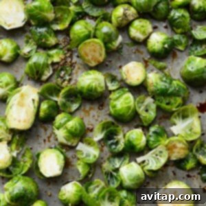 Balsamic and olive oil coated Brussels sprouts spread evenly on a baking sheet for optimal roasting.