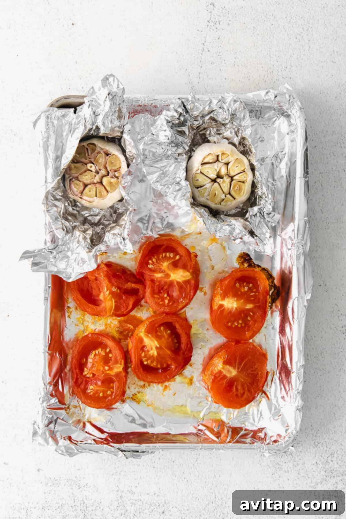 Roasted tomatoes and garlic cloves on a baking sheet