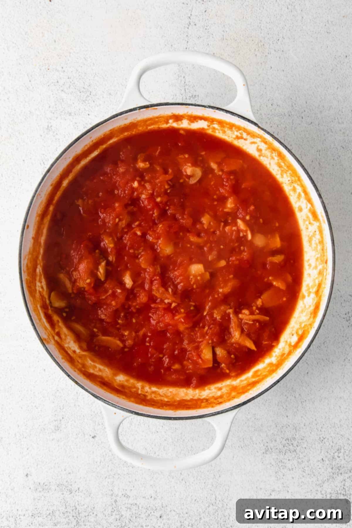 Rich pasta sauce simmering in a Dutch oven with roasted tomatoes, garlic, and spinach