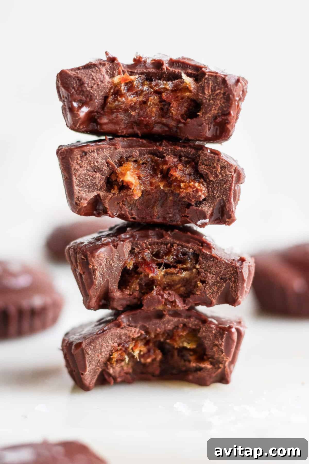 A stack of homemade salted caramel date cups, resembling decadent chocolate cups, with one bite enticingly taken out.