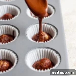A spoon applying the final layer of luscious melted chocolate over date caramel centers nestled in muffin cups, completing the assembly.