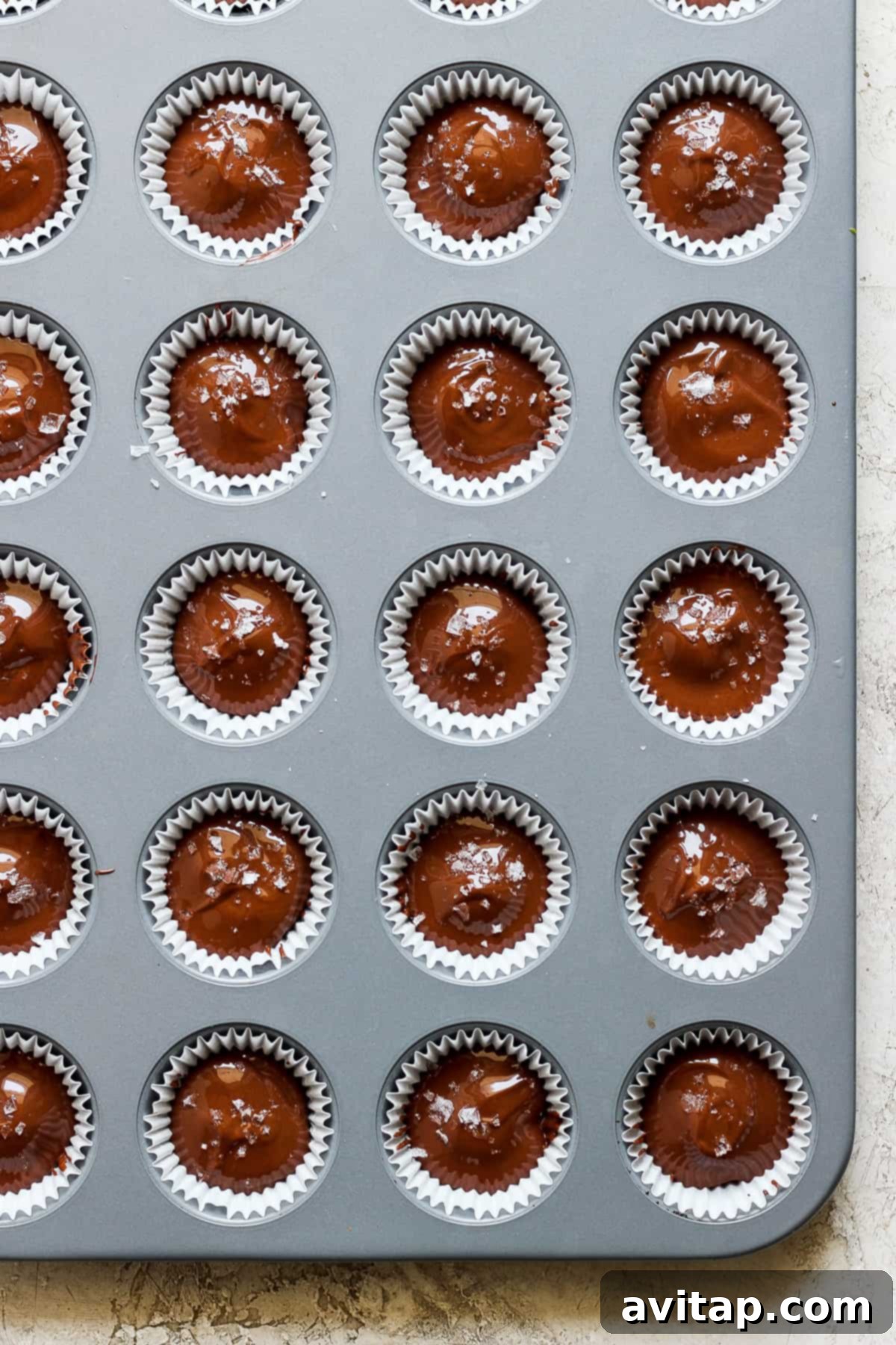 A muffin tin showcasing perfectly set salted caramel date cups, sprinkled with sea salt, ready to be enjoyed as a healthy and delicious snack.