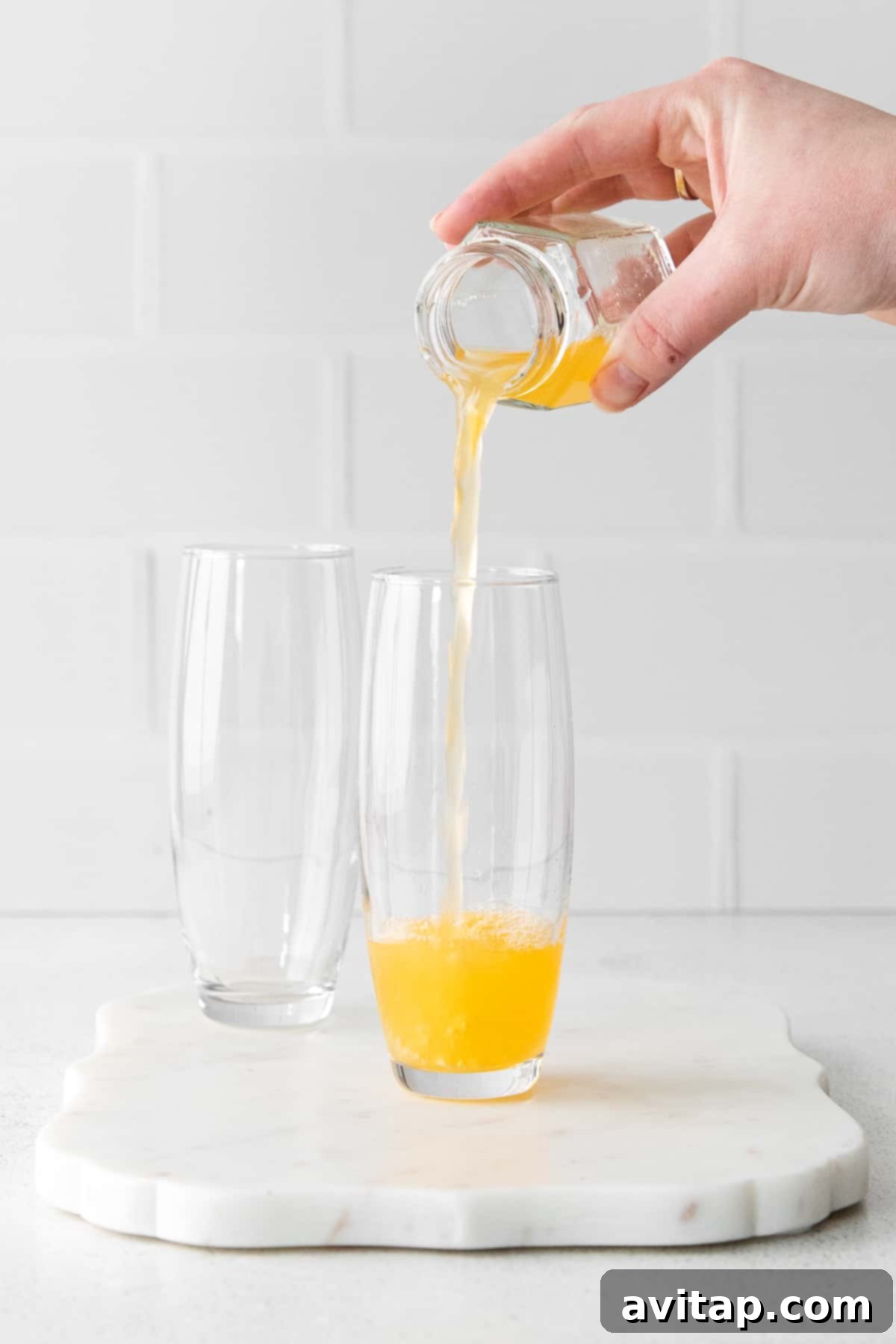 Fresh orange juice being carefully poured into elegant stemless champagne flutes, preparing for the sparkling wine.