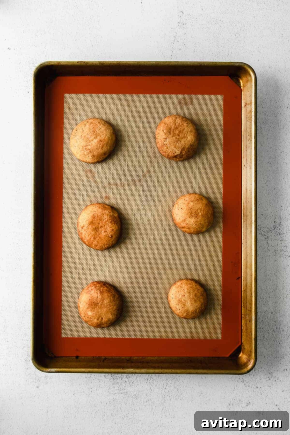Snicker doodles freshly baked on a baking sheet, glowing golden brown.