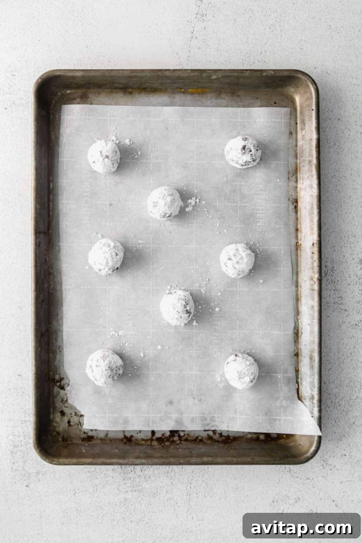Chocolate Crinkle Cookie Dough Ready for Baking Balls of chocolate crinkle cookie dough, coated in sugar, neatly arranged on a parchment-lined baking sheet, ready for the oven.