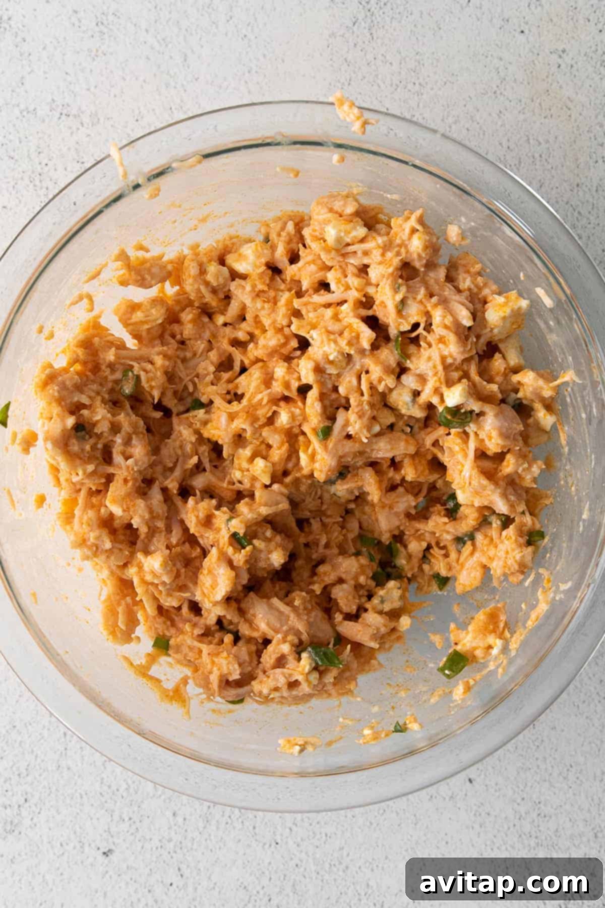 Shredded chicken being tossed with the freshly made buffalo sauce in a large bowl, ready for the next step.