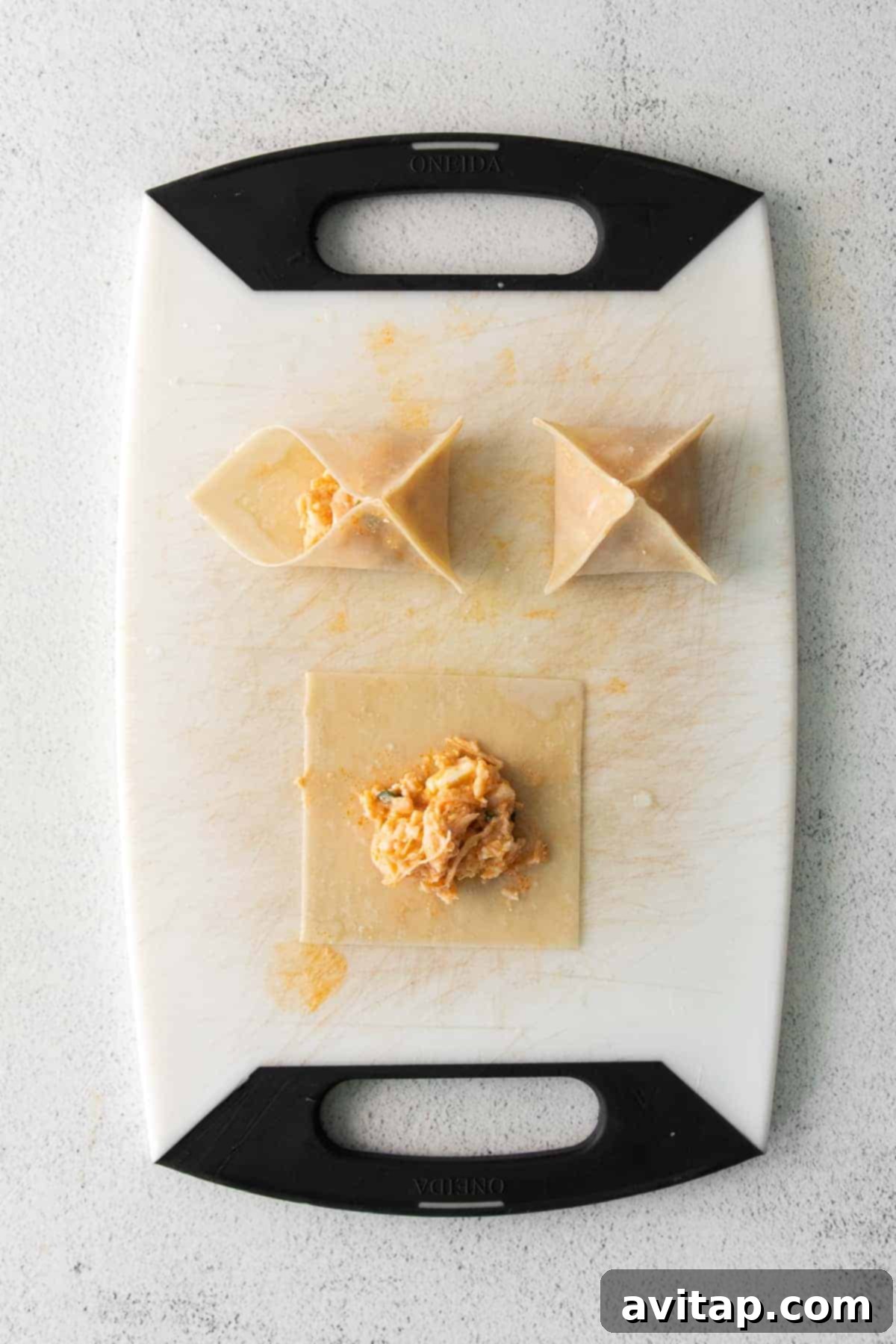 Wonton wrappers laid out on a cutting board, being filled with the buffalo chicken mixture, ready for folding.