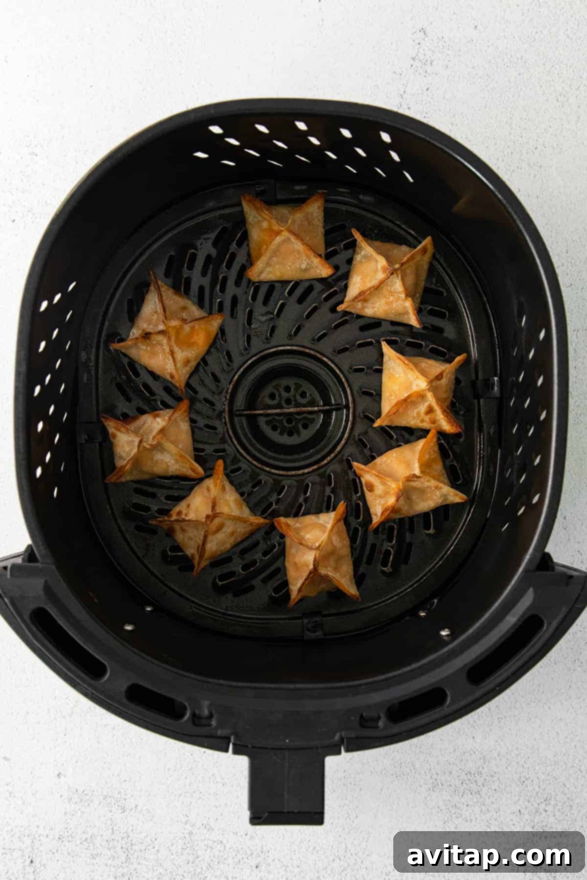 Buffalo chicken wontons arranged in an air fryer basket, lightly sprayed with oil, ready for cooking.
