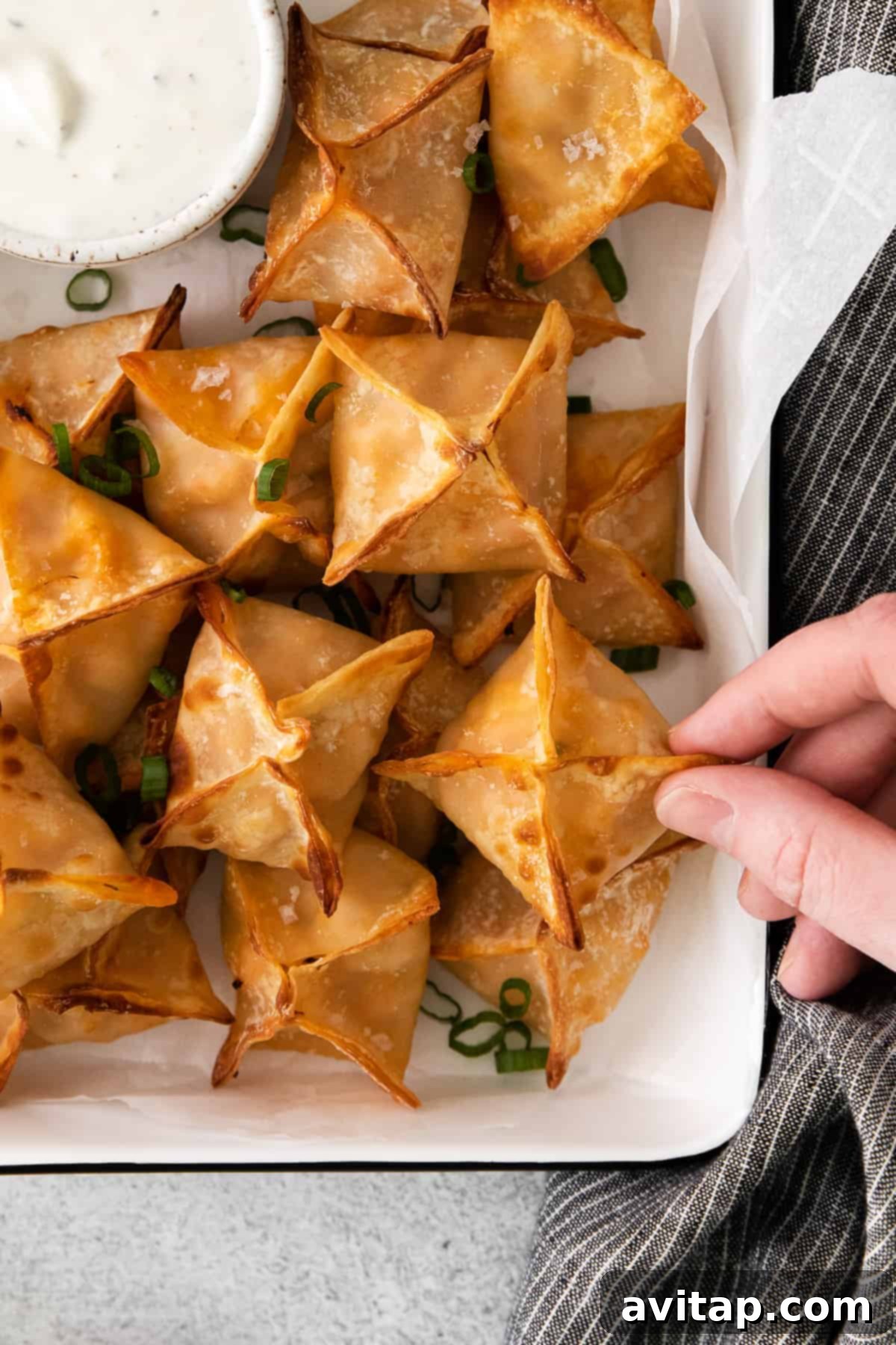 Freshly air-fried buffalo chicken wontons piled high in a container, garnished with green onions and ready to serve.