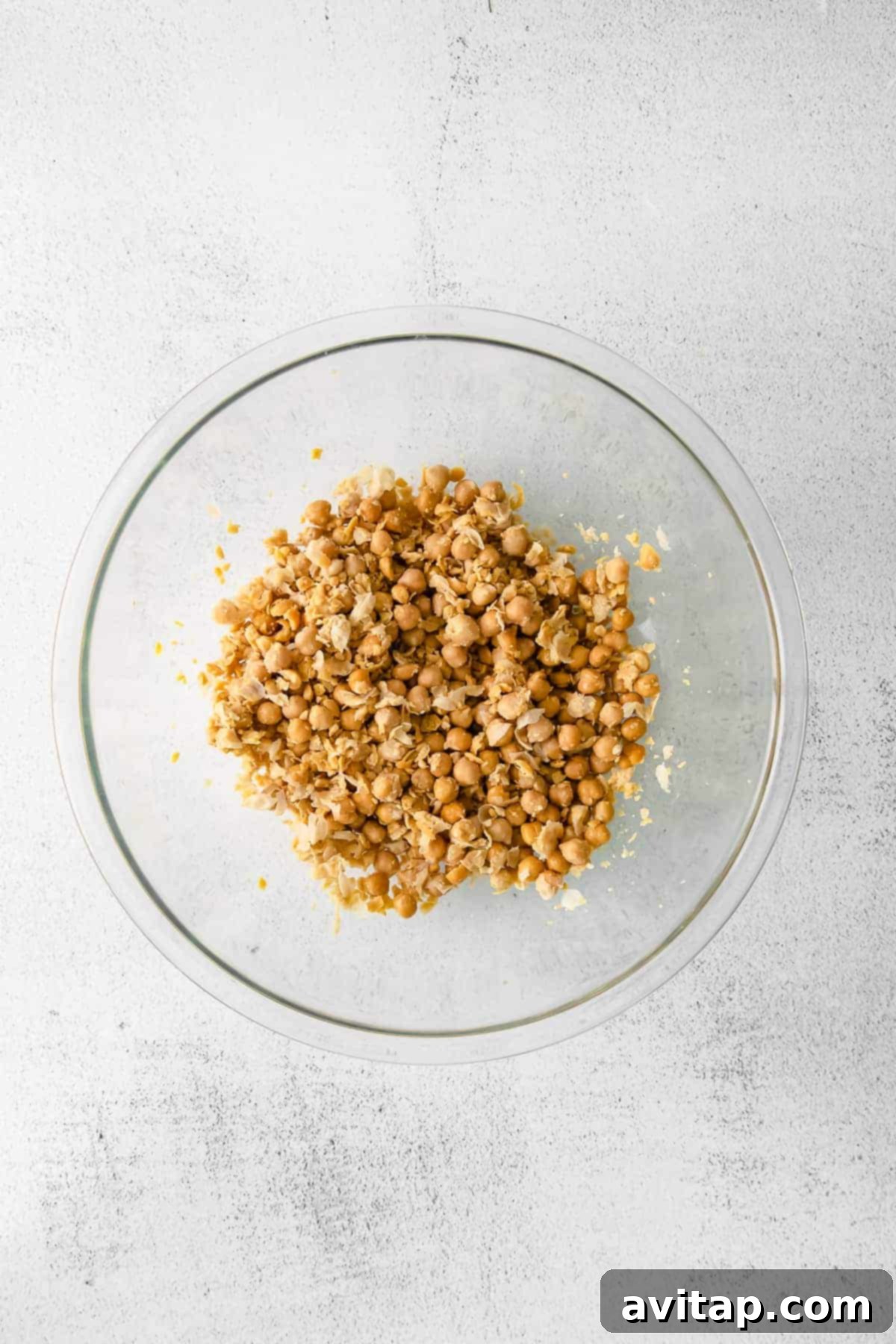 Mashed garbanzo beans in a mixing bowl, showcasing a creamy yet slightly chunky texture, indicating successful casing removal.