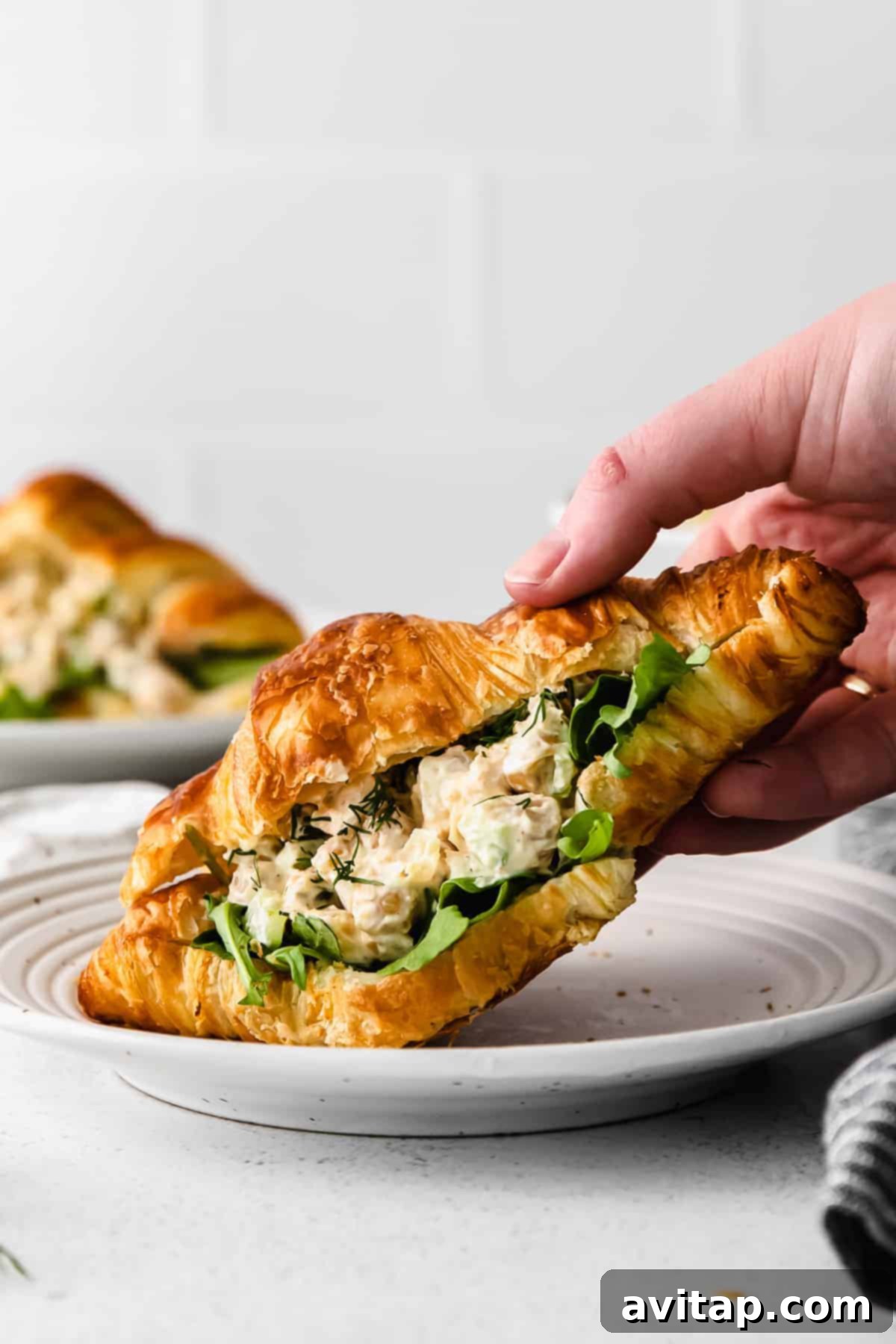 A close-up of a perfectly constructed chickpea salad sandwich on a golden croissant, highlighting the creamy filling and fresh ingredients, ready for a delicious bite.