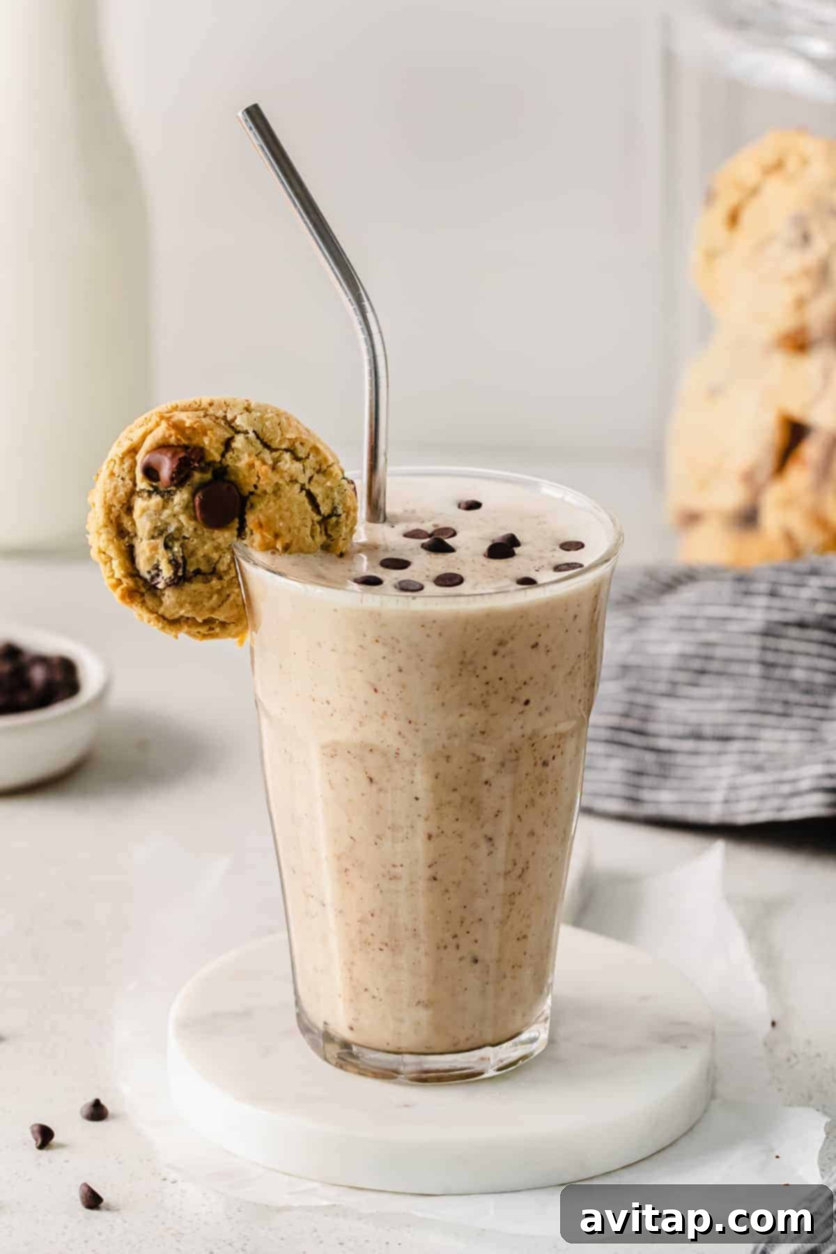 Decadent Chocolate Chip Cookie Dough Smoothie 2 A tall glass filled with creamy cookie dough smoothie, topped with mini chocolate chips, and a chocolate chip cookie perched on the rim, inviting a taste.