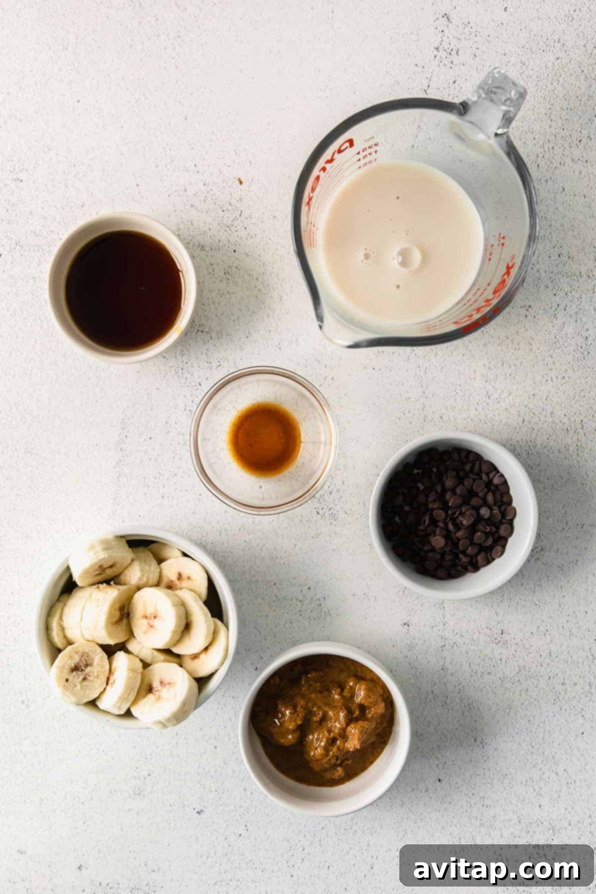 Decadent Chocolate Chip Cookie Dough Smoothie 3 An overhead shot showcasing all the simple ingredients for a chocolate chip cookie dough smoothie neatly arranged in small bowls on a wooden surface.