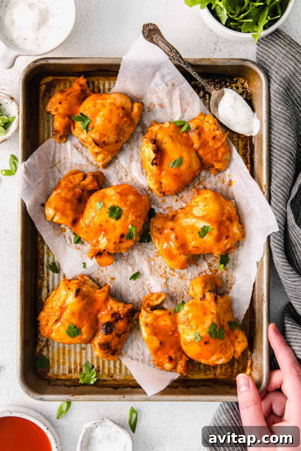 Super Juicy Baked Boneless Buffalo Chicken Thighs buffalo baked boneless chicken thighs on a baking sheet, garnished with fresh herbs