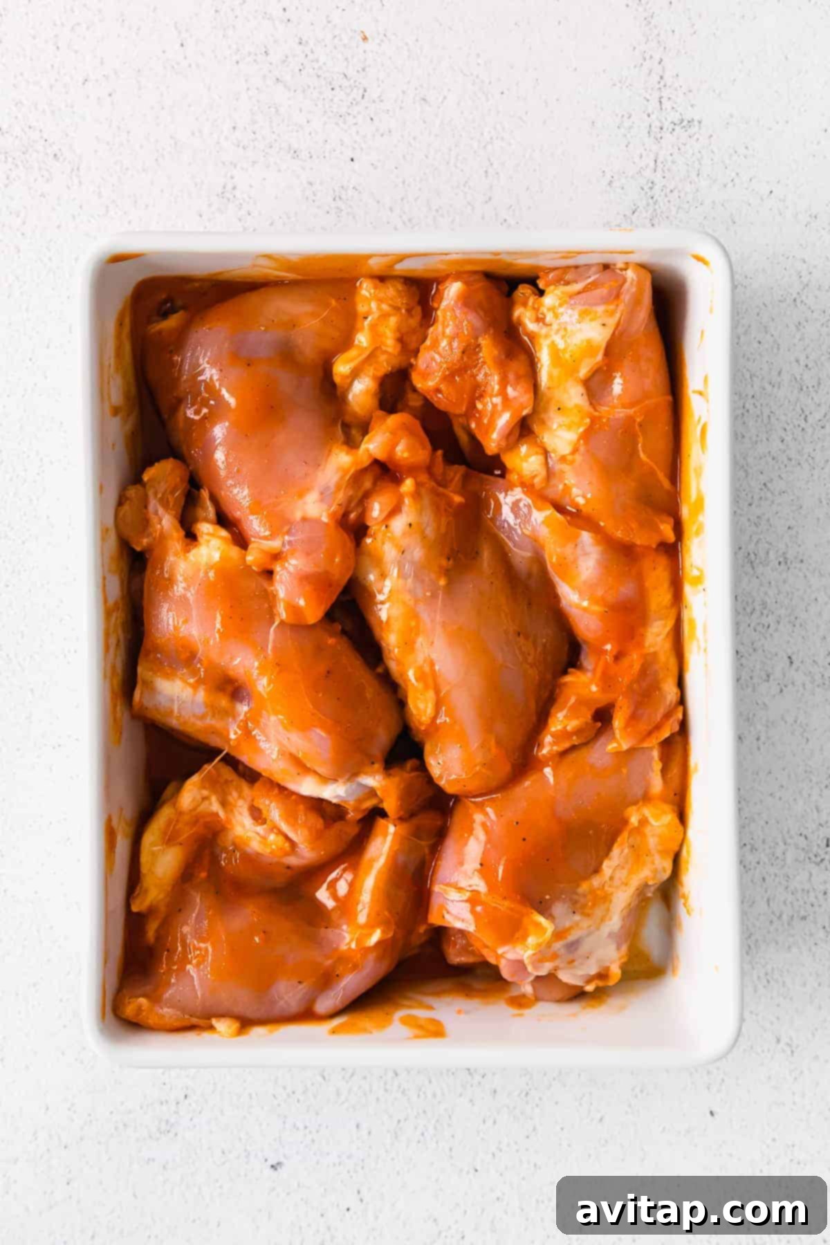 Marinating Boneless Chicken Thighs raw boneless chicken thighs marinating in buffalo sauce in a casserole dish