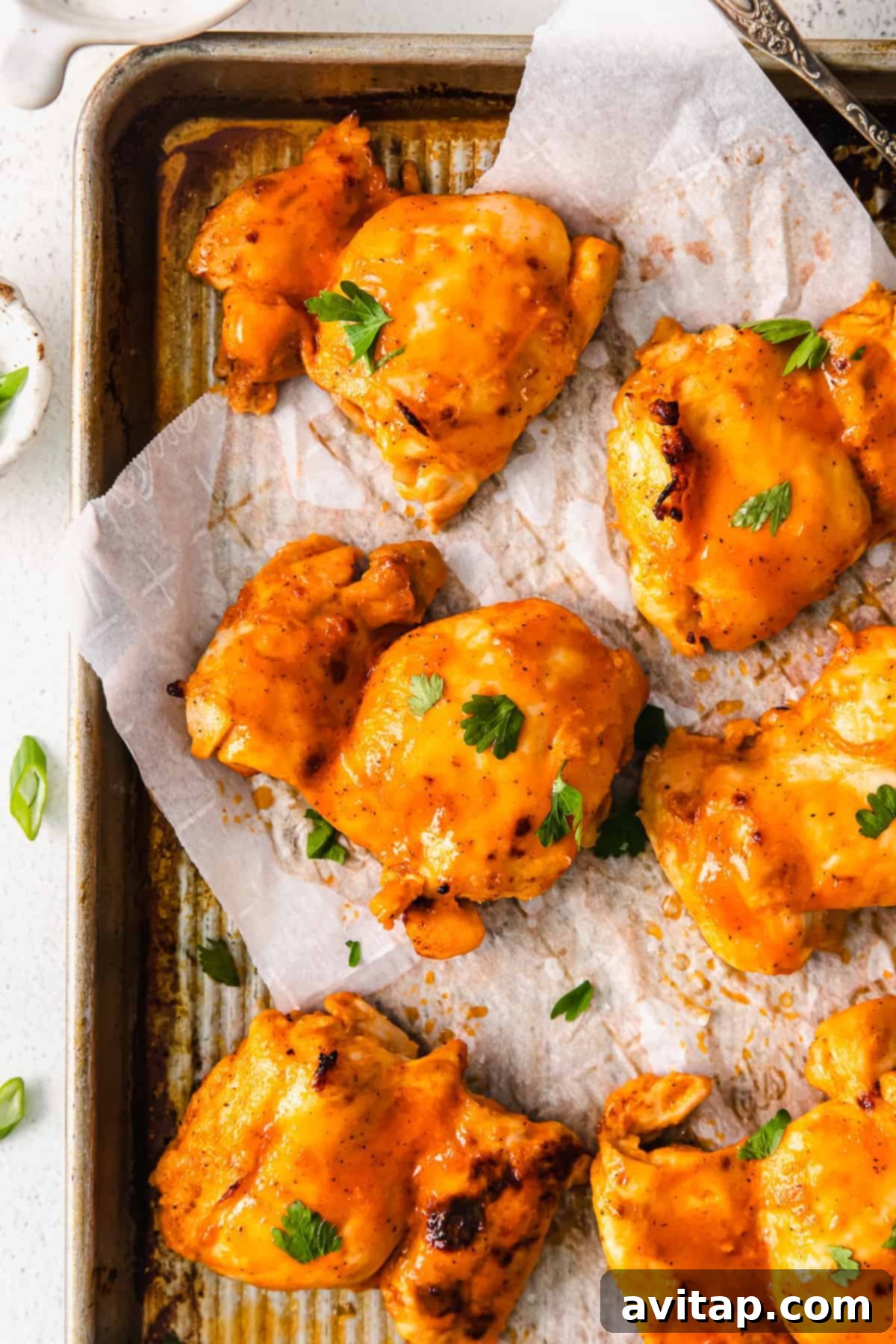 Finished Buffalo Baked Chicken Thighs buffalo baked chicken thighs on a baking sheet, garnished with fresh parsley