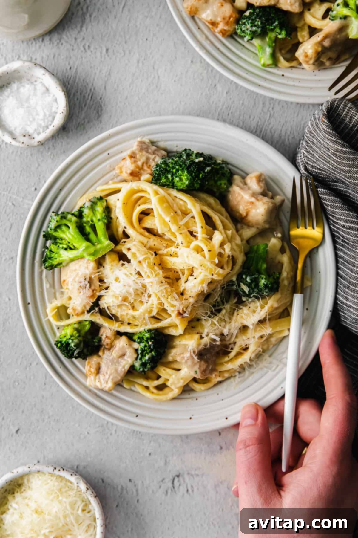 A plate of chicken broccoli alfredo, garnished with fresh parsley and grated parmesan, ready to be enjoyed.