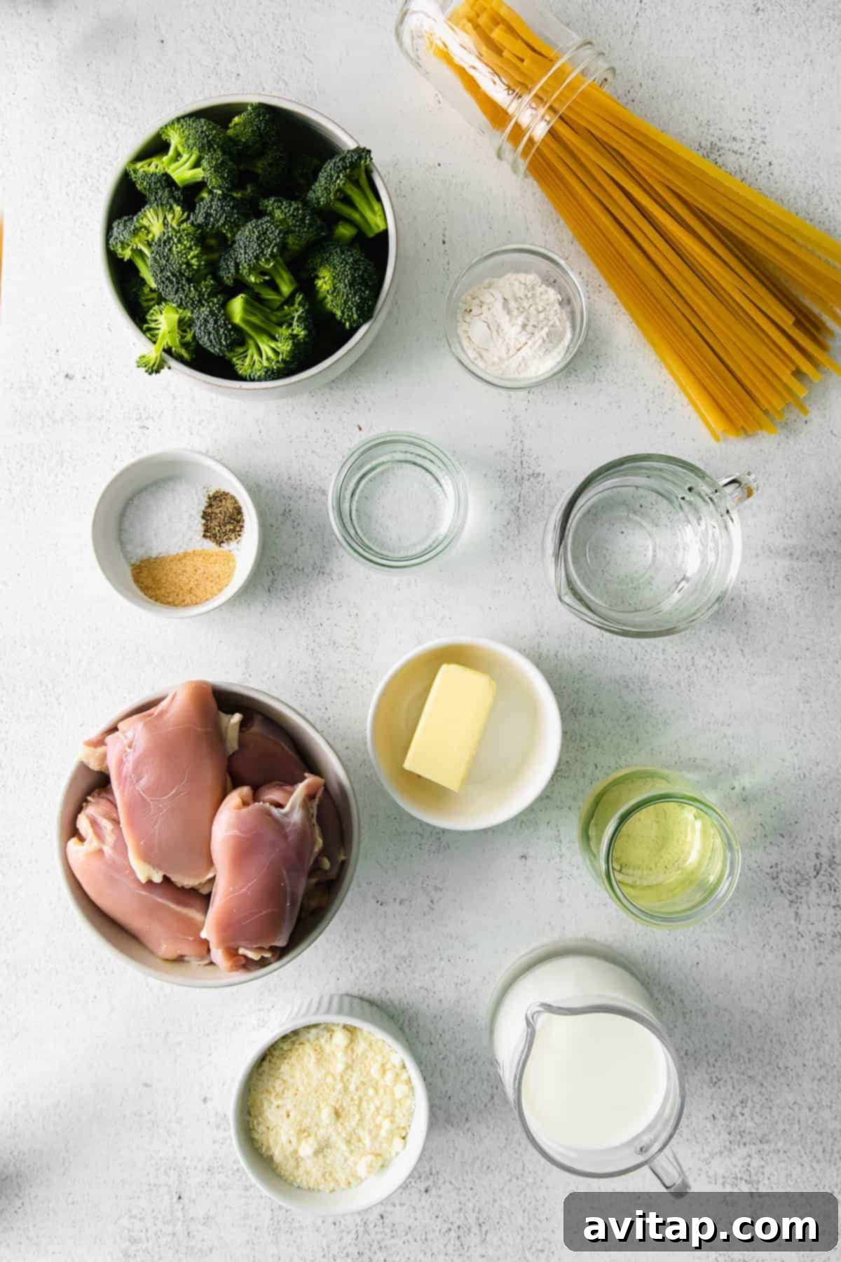 Various ingredients for chicken broccoli alfredo, including chicken thighs, butter, parmesan, garlic, and milk, displayed in small bowls.