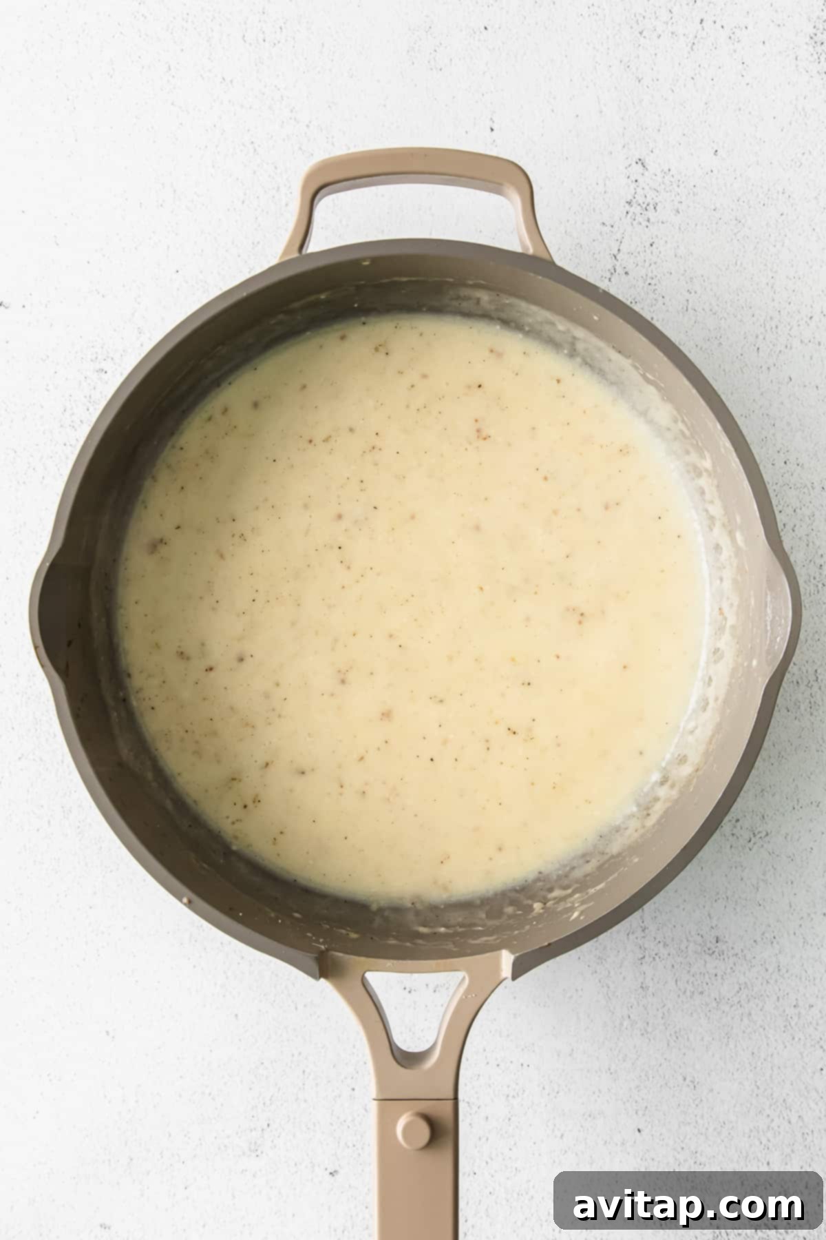 Creamy alfredo sauce bubbling gently in a pan, ready for pasta and protein.