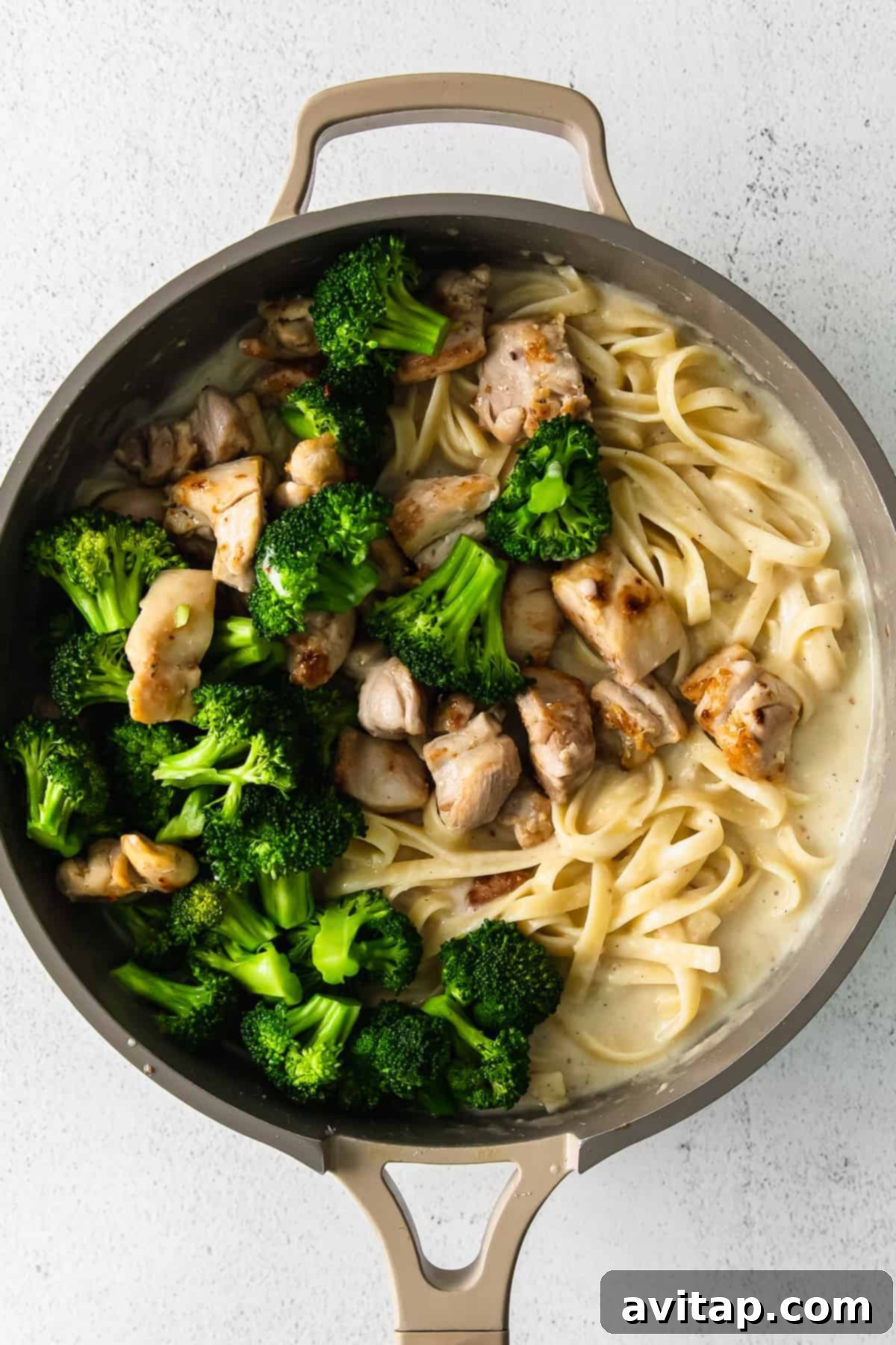 A large skillet brimming with chicken, broccoli, and fettuccine noodles, all coated in a rich, creamy alfredo sauce.