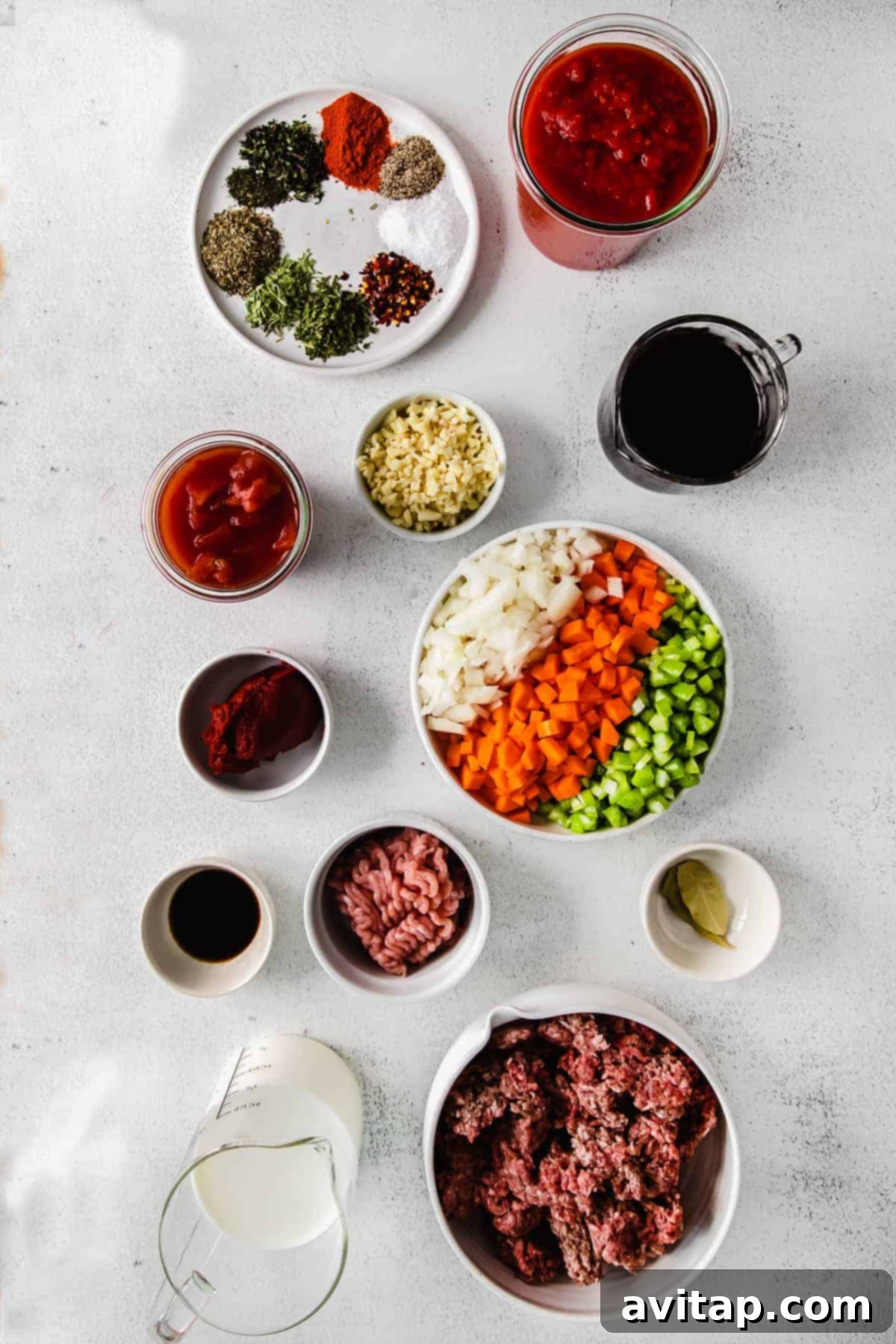 Key Ingredients for Slow Cooker Bolognese A selection of fresh ingredients laid out on a counter, ready for making slow cooker bolognese: ground meats, vegetables, spices, wine, milk, and canned tomatoes.