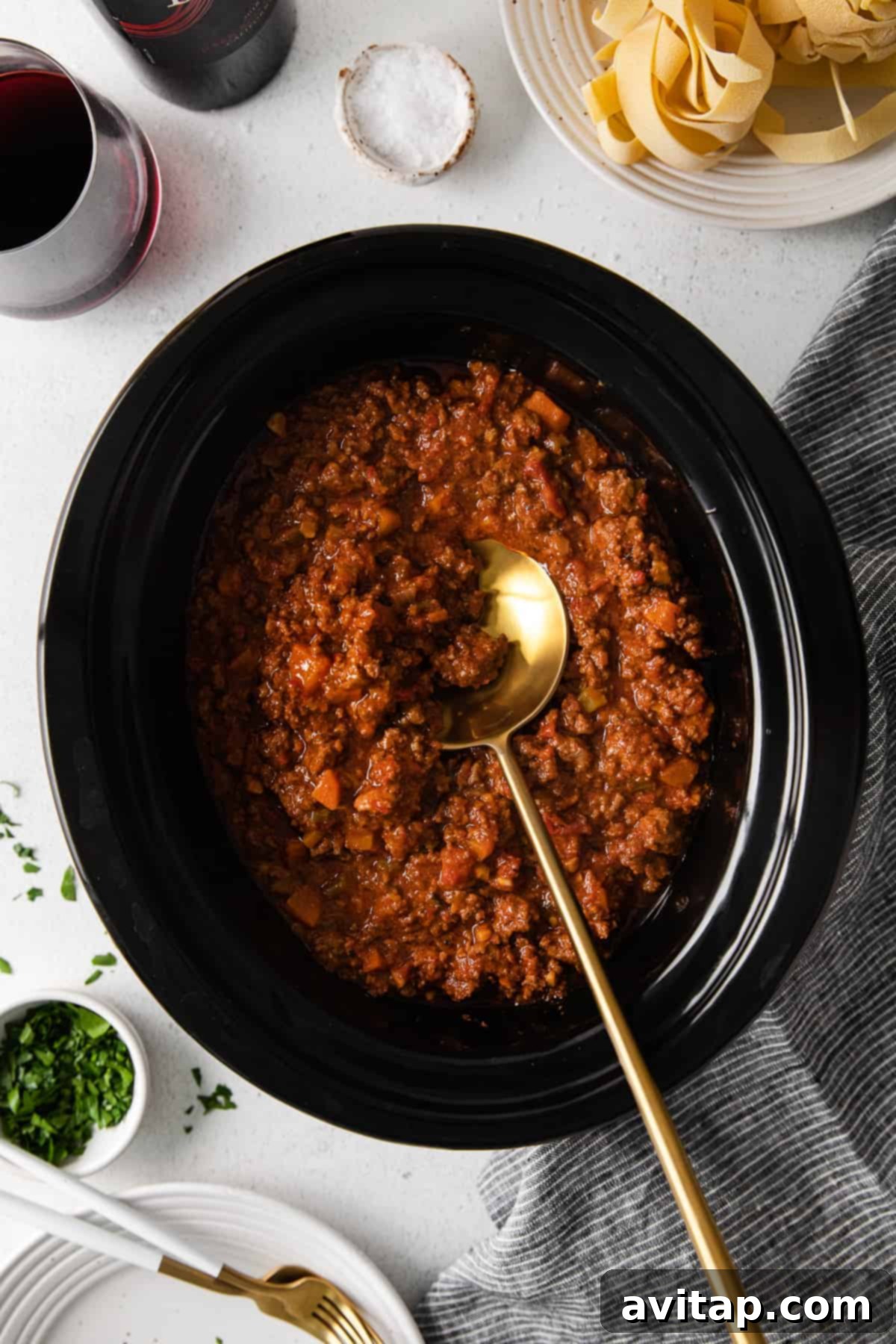 Slow Cooker Bolognese Perfection Rich and thick slow cooker bolognese sauce simmering in the slow cooker with a wooden spoon, indicating it's almost ready.