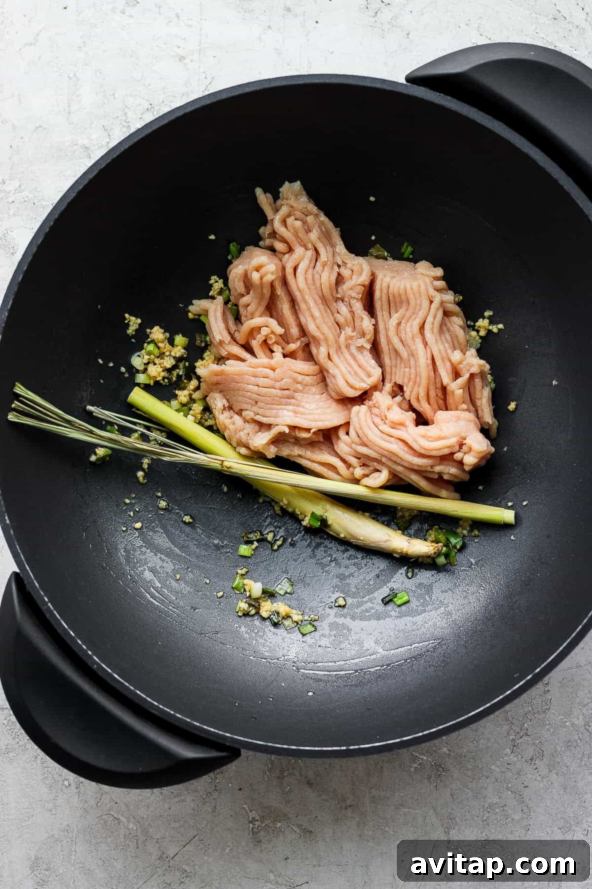 Sautéing Ground Chicken and Aromatics for Thai Basil Stir Fry Close-up shot of seasoned ground chicken browning in a hot wok, mixed with aromatic garlic, shallots, and broken lemongrass stalks, forming the flavorful base for Pad Krapow.