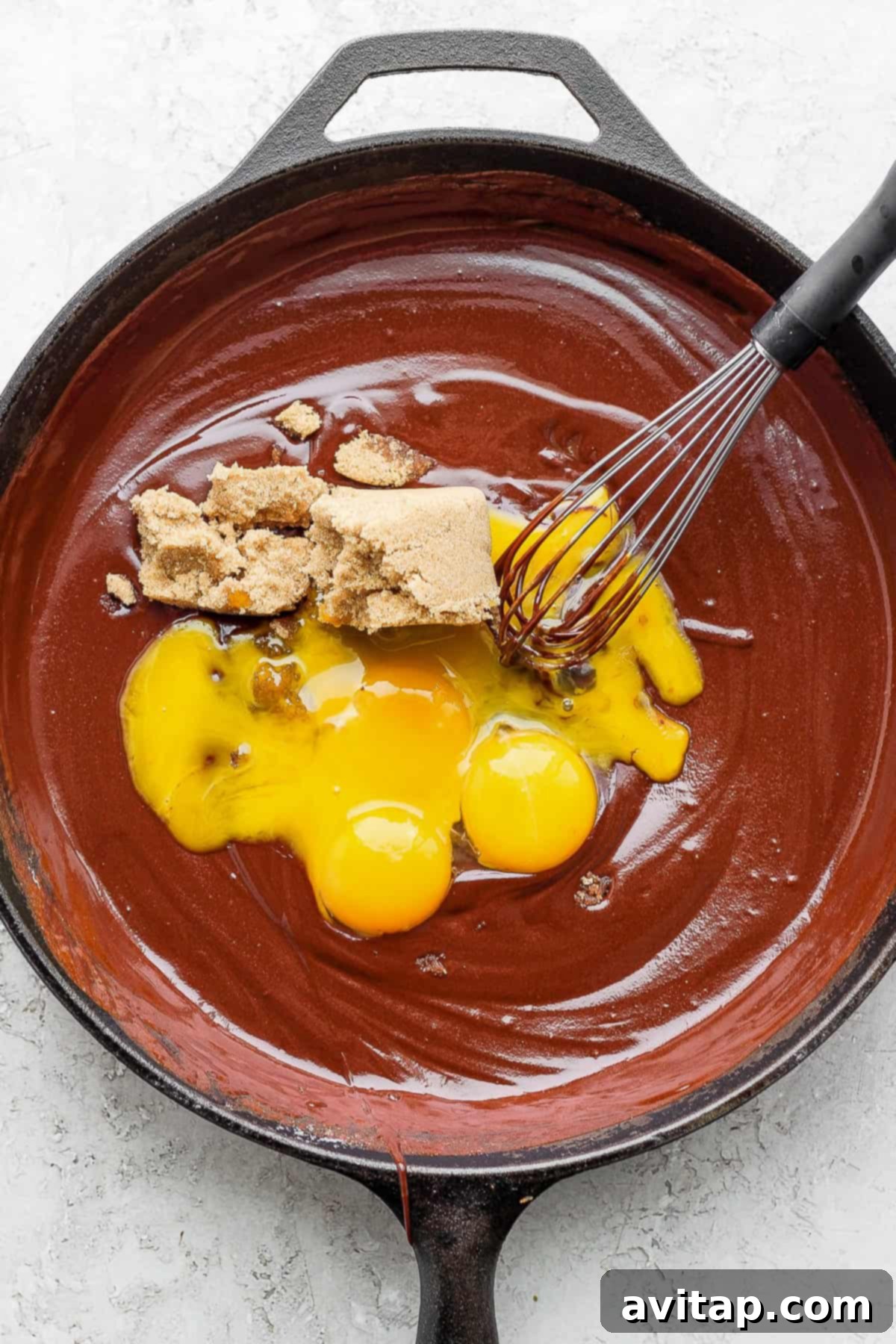 Adding Yolks and Sugar to Chocolate Egg yolks and light brown sugar being added to the melted chocolate and butter mixture in a cast iron skillet, ready to be whisked into a creamy batter.