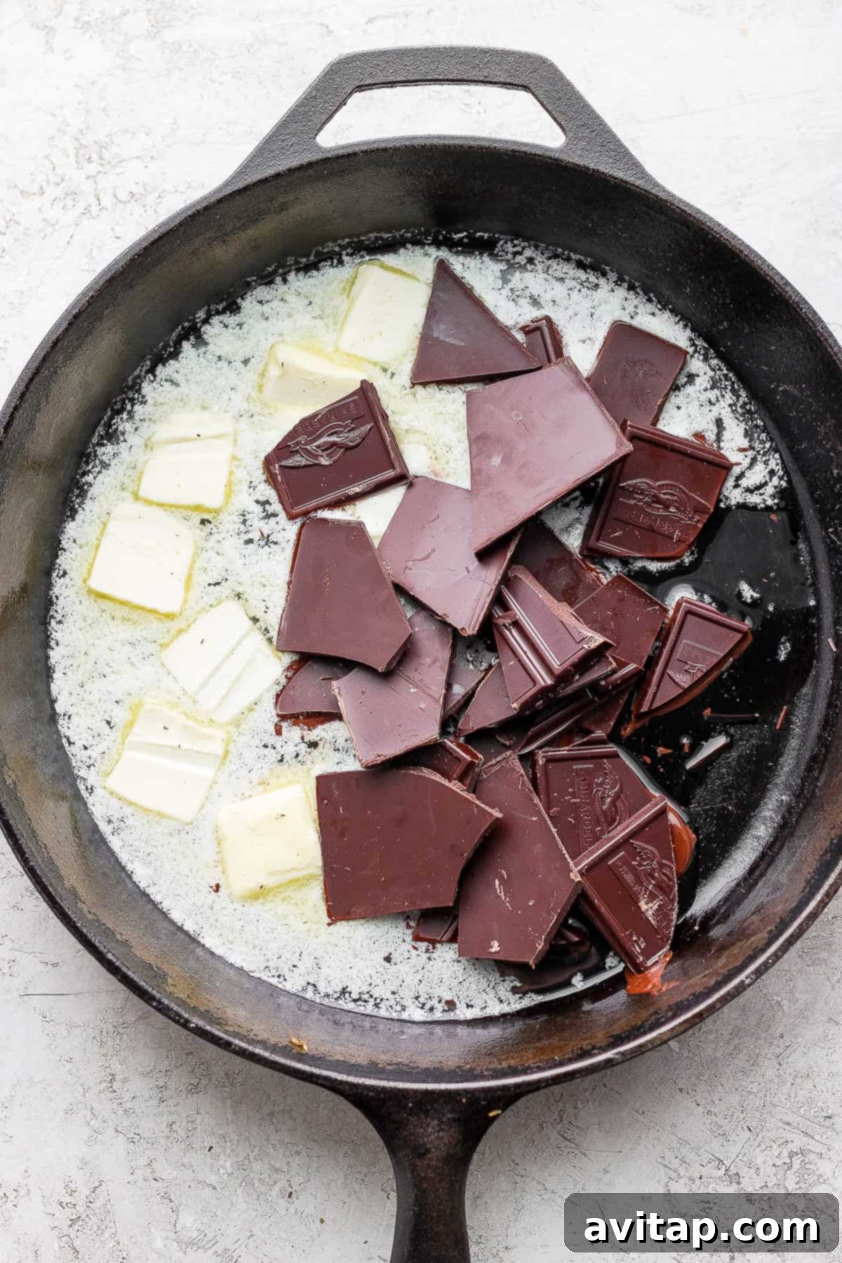 Melting Chocolate and Butter Base Close-up of bittersweet chocolate chunks and unsalted butter cubes gently melting together in a hot cast iron skillet, becoming glossy and smooth.