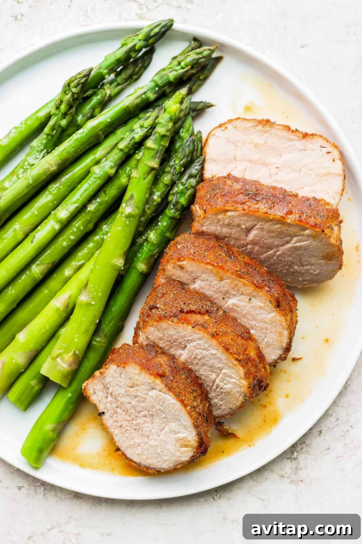 Air fryer pork tenderloin on a plate with fresh asparagus, showcasing a perfectly cooked and sliced tenderloin with a golden crust.