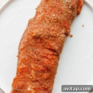 Pork tenderloin on a plate, generously coated with a savory dry rub, ready for air frying.