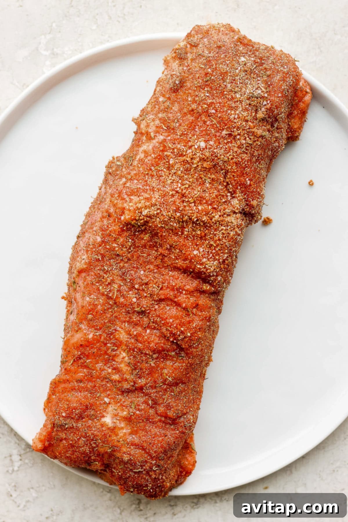 Pork tenderloin on a plate, generously coated with a savory dry rub, ready for air frying.