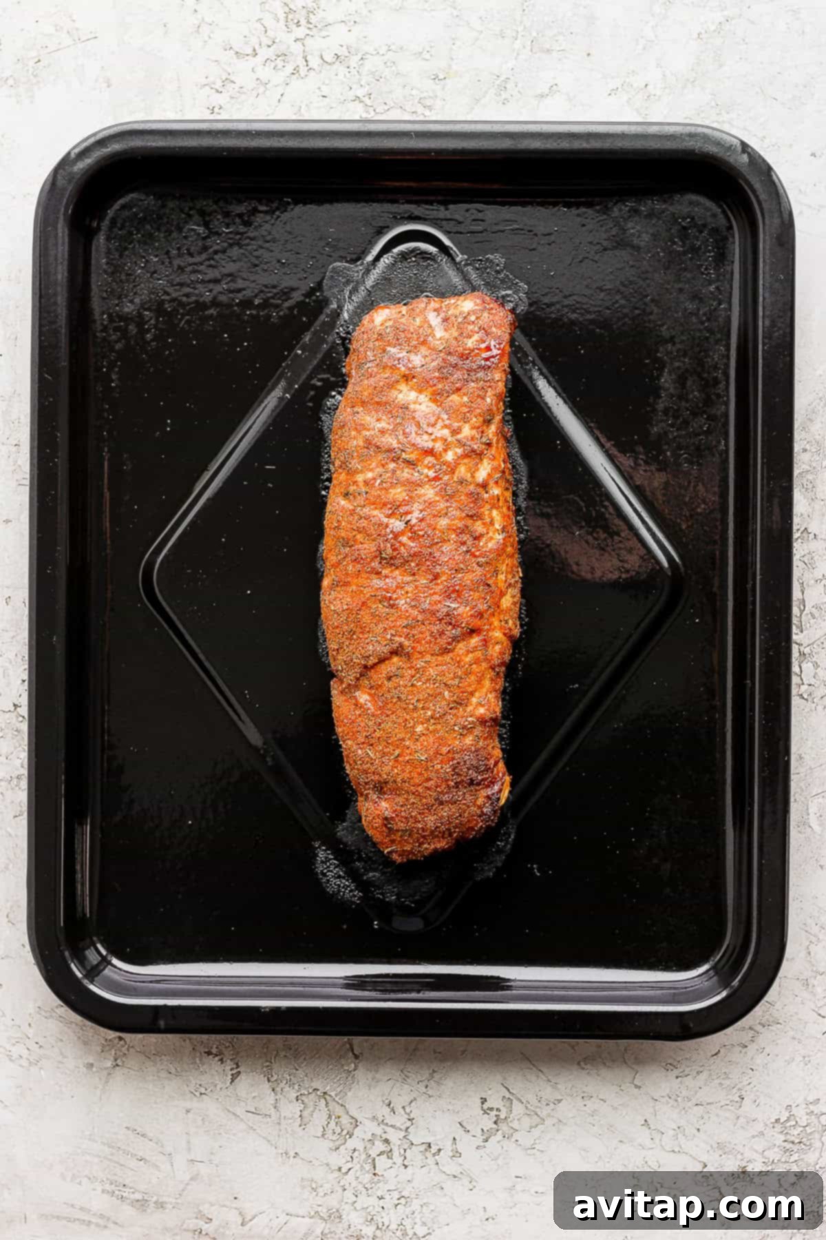 Air fryer pork tenderloin resting on the air fryer rack after cooking, showcasing its perfectly golden and crispy surface.