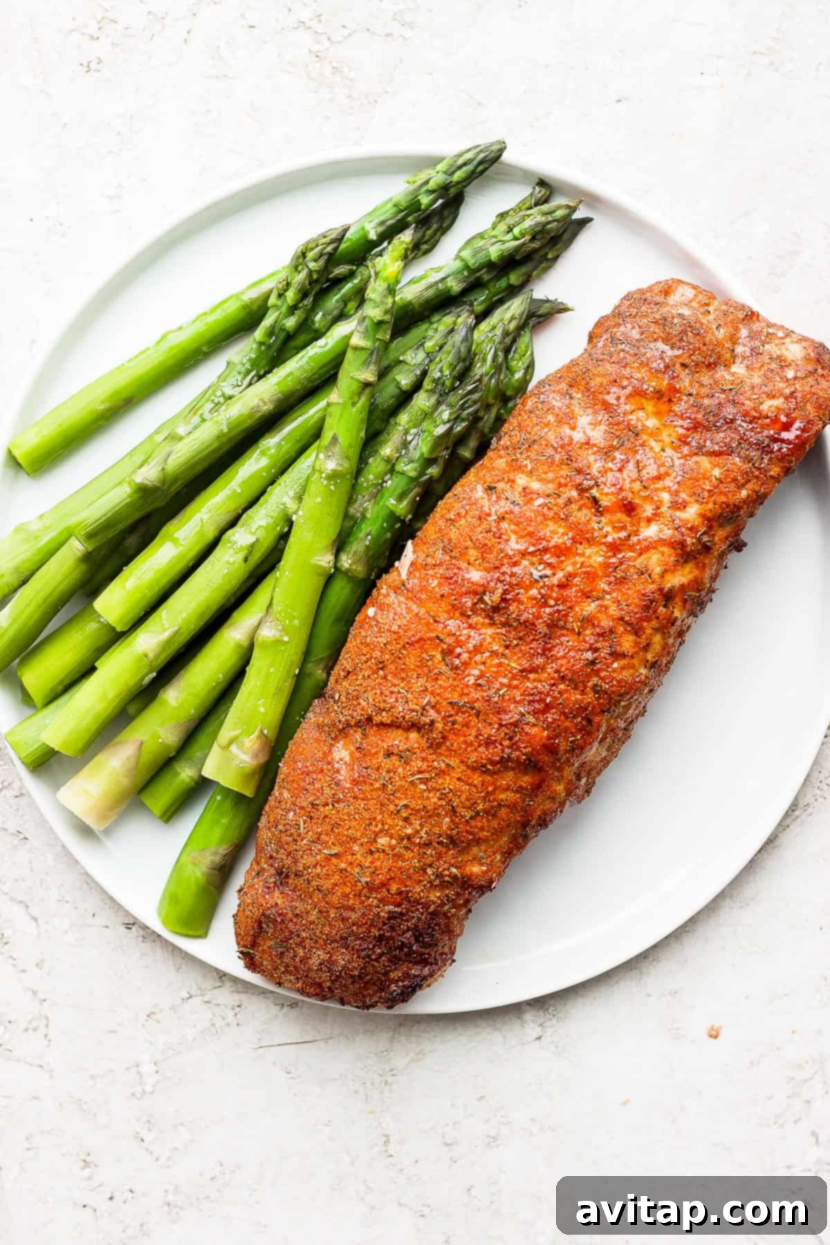 Cooked air fryer pork tenderloin served on a plate with asparagus, perfectly golden brown and ready to eat.