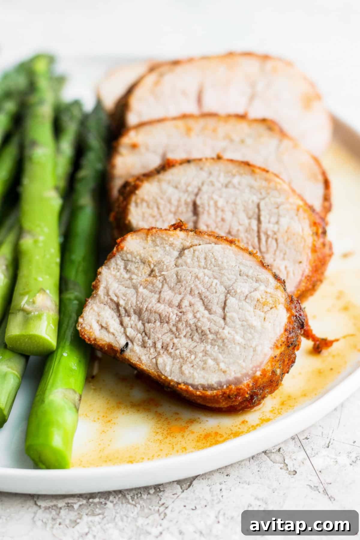 Air fryer pork tenderloin sliced into medallions and arranged on a white plate, revealing its juicy interior.