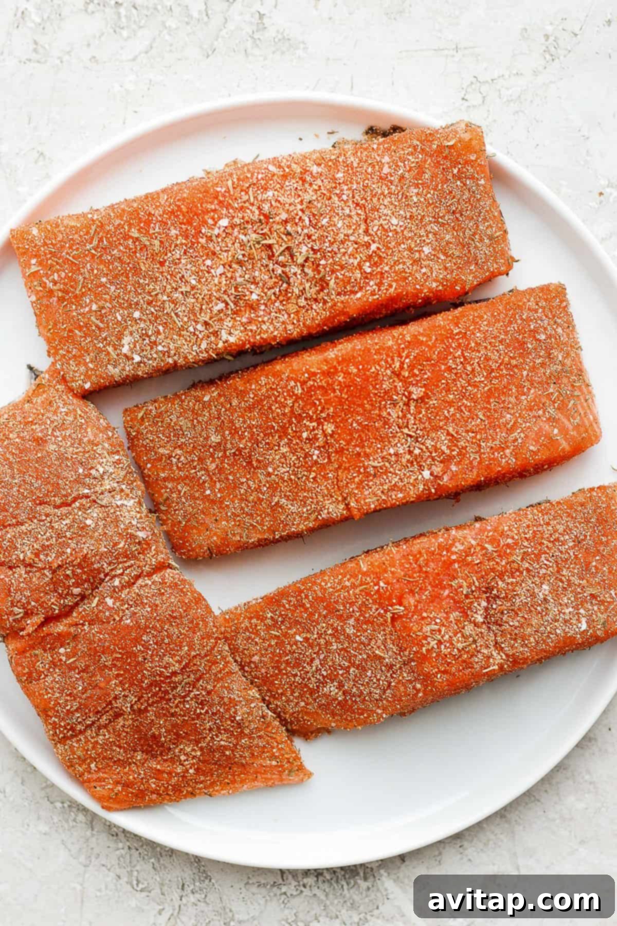 Make your own Homemade Salmon Seasoning with just 7 ingredients you likely already have in your spice cupboard, and you’ll be on your way to the most flavorful salmon in no time. Two perfectly seasoned salmon fillets on a white plate, showcasing the vibrant colors of the salmon seasoning rub before cooking.