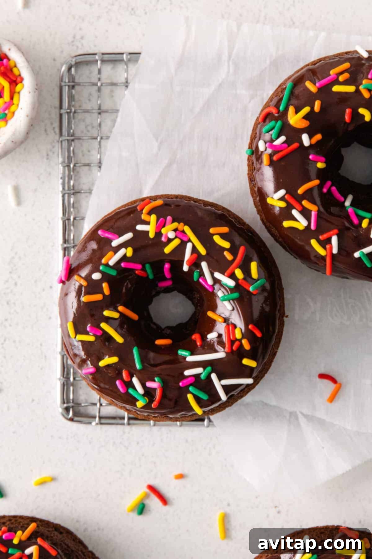 Freshly baked chocolate donut cooling on a wire rack, topped with chocolate frosting and colorful sprinkles.