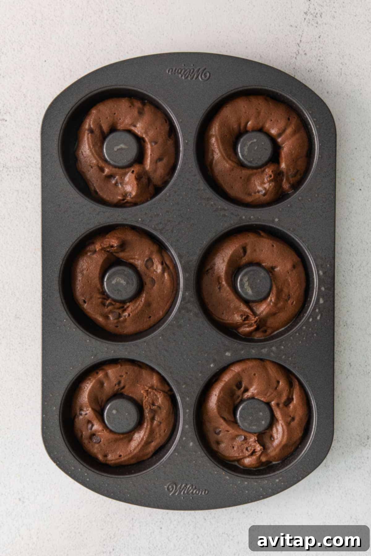 Chocolate donut batter precisely piped into a greased donut mold, ready for baking.