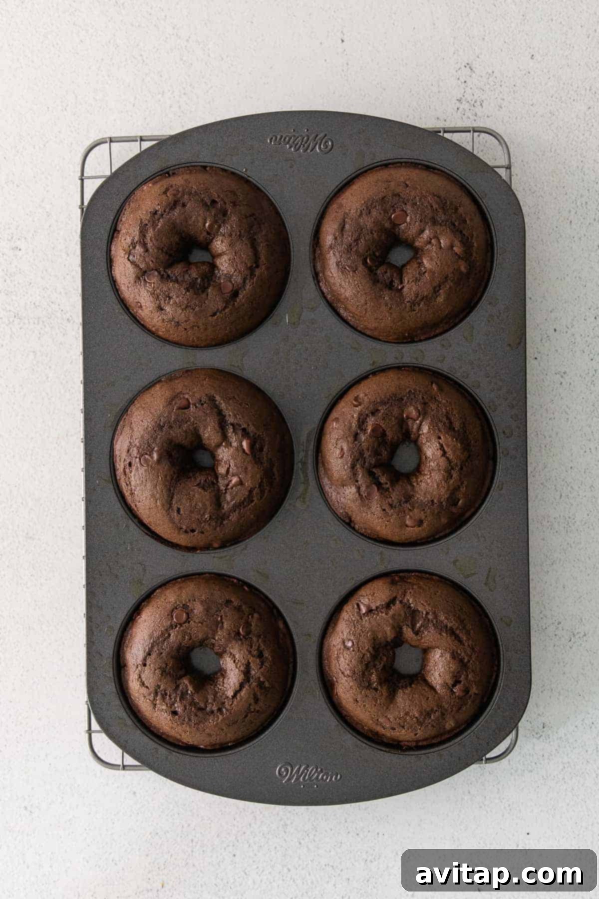 Baked chocolate donuts cooling in a donut pan on a wire rack.