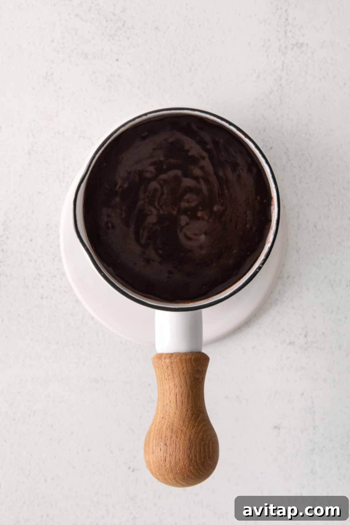 Smooth, shiny chocolate glaze in a small bowl, ready for dipping donuts.