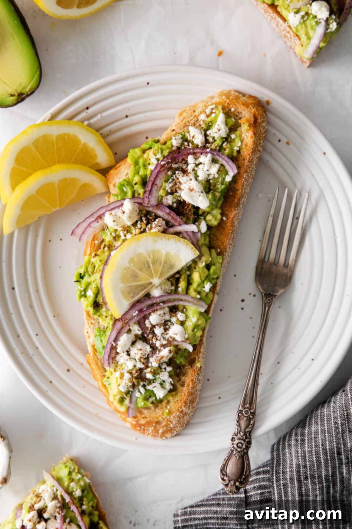Mediterranean avocado toast on a plate, garnished with feta, red onion, and lemon
