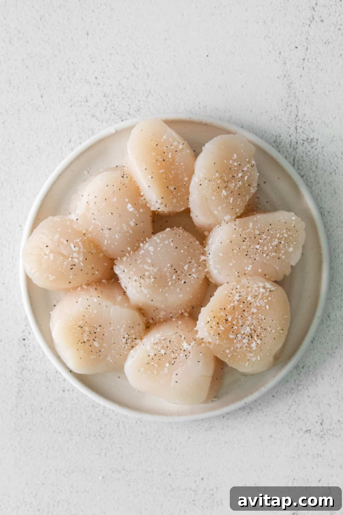Seasoned scallops on a plate, ready for searing. 