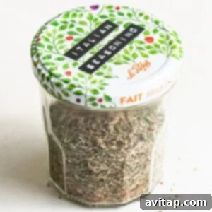 A jar of homemade Italian seasoning on a white surface, ready for storage.
