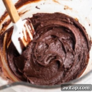Chocolate cake batter in a bowl with a wooden spoon.