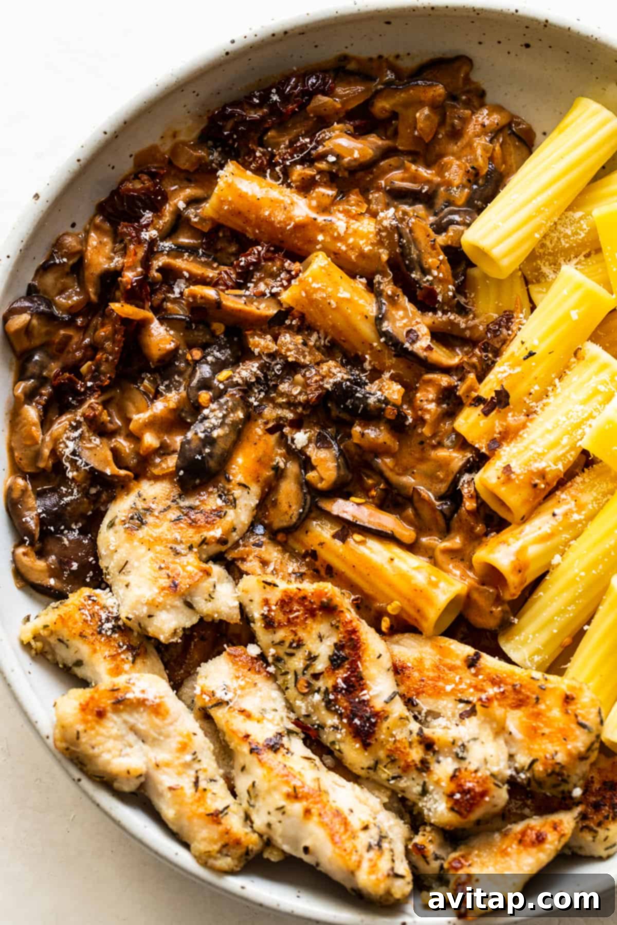 A serving of chicken mushroom pasta on a white plate, ready to be enjoyed
