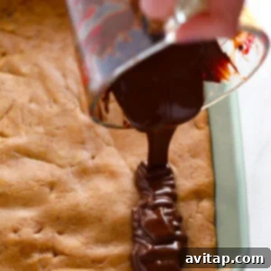 A person drizzling chocolate over a peanut butter protein bar base in a pan.