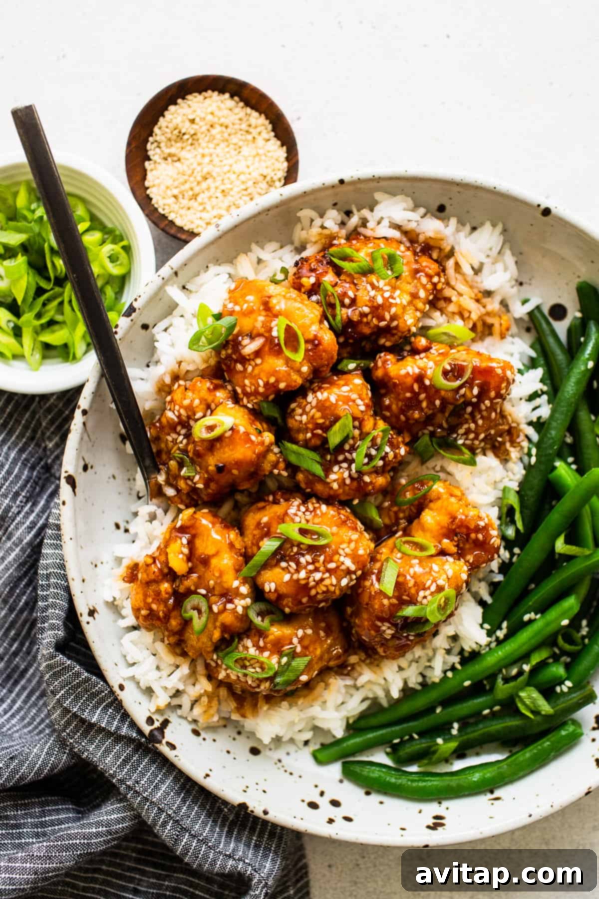 A bowl of sesame chicken served with green beans and other vegetables.