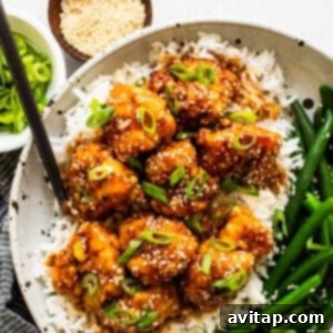 A vibrant bowl of honey sesame chicken, served with rice and green beans, garnished with fresh green onions and sesame seeds.